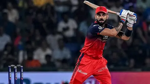 Virat Kohli, wearing a cap, plays a shot for RCB
