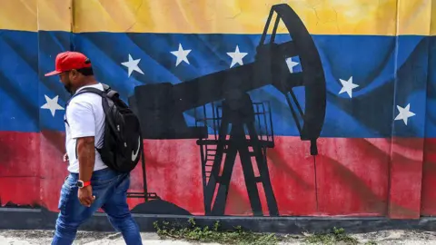 AFP via Getty Images A man walks past a mural depicting an oil pumpjack on a Venezuelan flag in Caracas 