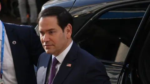 US. Secretary of State Marco Rubio arrives at the 61st Munich Security Conference on 15 February. He is wearing a dark coloured suit, a blue and red patterned tie and a pin on his lapel of the American flag 