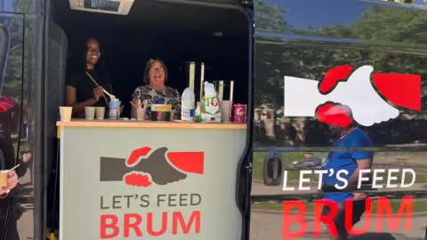 A young woman and an older woman smile at the camera. They stand behind a counter in a van and serve drinks. A logo on the van and the counter shows two hands grasping each other above the words 'Let's Feed Brum'.