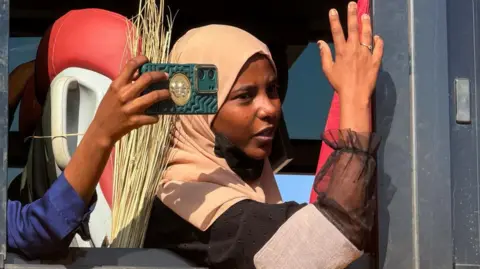 A woman wearing a headscarf, sits by a window of a bus. 