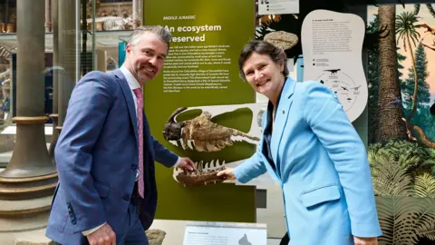 Fisher Studios and Museum of Natural History, University of Oxford Dr Gavin Svenson and the Vice Chancellor smiling as they install the final exhibit of Megalosaurus jaw bone at the Museum of Natural History.