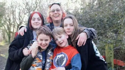 Family handout Emily smiling for a photo with all four of her children outside.