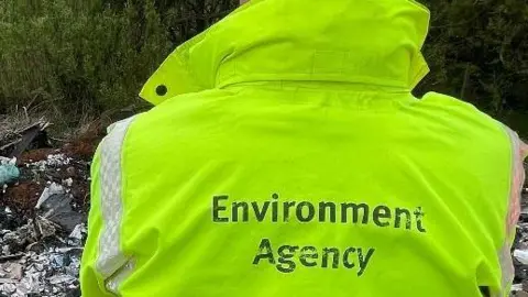 Environment Agency officer with his back to camera. Wearing neon jacket reading 'Environment Agency'. 