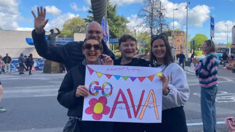 A family holds up a sign saying "go Ava" 