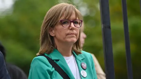 PA Media Lyra McKee's sister Nichola is wearing a green jacket and is speaking into a microphone outside court. She has sandy coloured hair and glasses. 