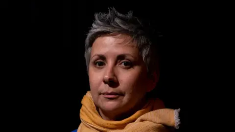 Phil Miller Isabelle Defaut has grey hair and wears a yellow scarf 