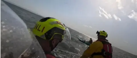 RNLI Barry Dock A picture from the rescue taken from the RNLI boat. Two crew members can be seen wearing RNLI helmets and lifejackets. In the background Marley can be seen on top of the kayak in the sea. 