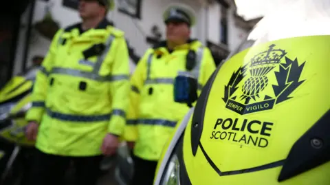 PA Media This image shows a fluorescent yellow Police Scotland motorbike which shows a black emblem which reads 'Semper Viglo'. Two officers wearing high vis jackets are blurred in the background.