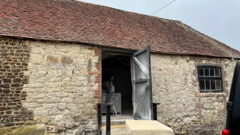 George Carden/BBC A barn with old bricks and red tiles with an open wooden door where the stonemasons work