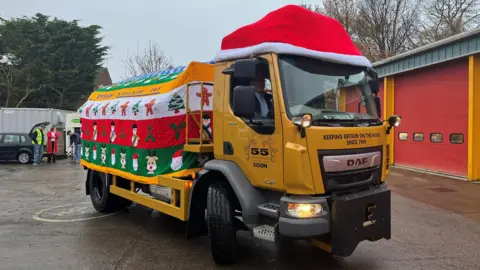 BBC/ Julia Lewis A yellow gritter covered in a "knitted jumper" and a Santa hat. Pictures of gingerbread men, reindeer and Santa make up the design.