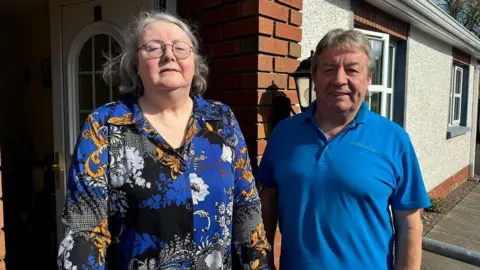 Breda Murphy standing with Fermanagh Community Transport driver Tony Harte outside her home