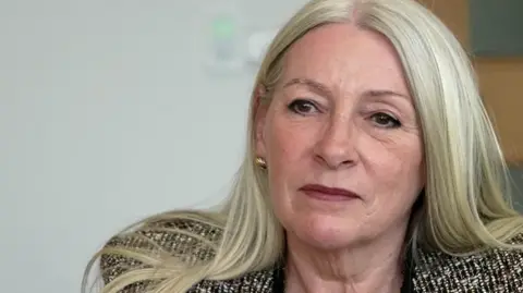 Kay Mason Billig is looking at the camera. We can see she's wearing a patterned suit jacket.