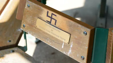 A close up of a black swastika drawn on a park bench in Bognor, above a brass plate saying "seating donated by Hotham Park Heritage Trust".