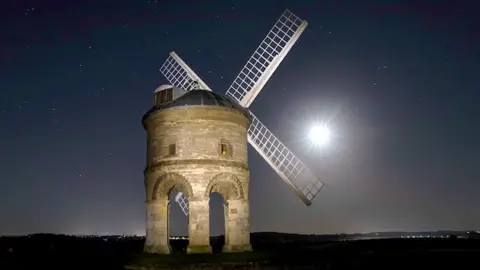 Damien Walmsley An ancient windmill captured at night. The bright moon is positioned between two of the white sails