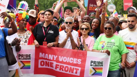 Getty Images London Mayor Sadiq Khan in the centre of the shot. In front of him is a banner which reads Pride in London/Many Voices One Front. Other people stood with him are singer Beverley Knight, Dawn Butler MP, Saadiya Khan and Mete Çoban MBE