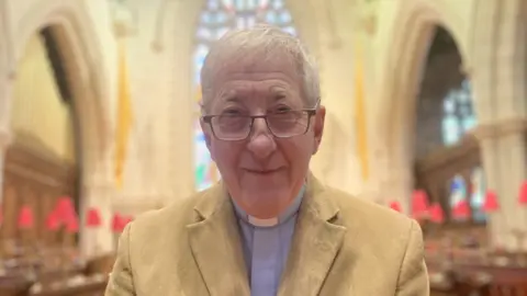 BBC Shows a clergyman in a light-coloured jacket with a minister's blue garb underneath