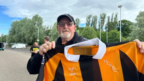 Matt Dean/BBC Gary Rumkee pictured with his shirt. He is wearing glasses and a cap and has a goatee beard.