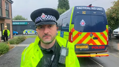 Photograph of Chief Inspector Lee Grindley from Greater Manchester Police. The image shows him in his police uniform, in front of a Tactical Aid Unit van.