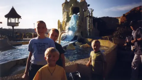 Anton Honchanka Anton on the left with a grey t shirt. He is stood next next to three boys and there is a attraction behind them at a waterpark. 