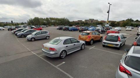 A large tarmac car park dotted with parked cars