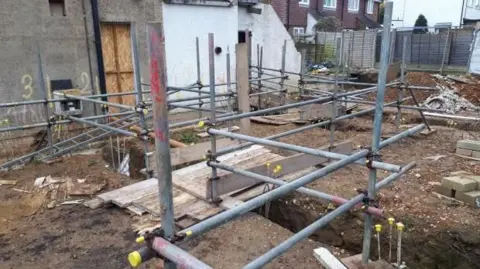 HSE A construction site during the foundation stage of a building project. A network of metal scaffolding and support frames has been erected across the site.