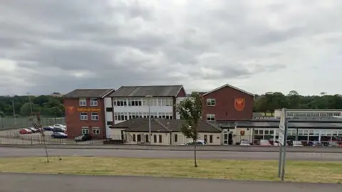 A Google street view screenshot of Netherhall School in Maryport. It is made up of several buildings, with a car park at the front and a sports pitch to the side.