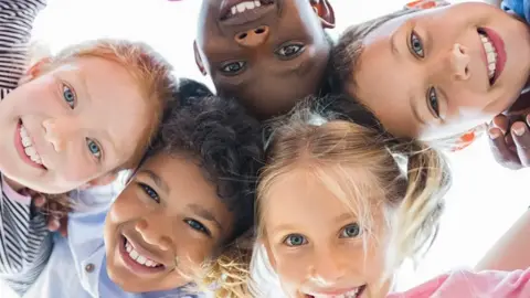 Getty Images Five children of different ethnicities look down into the camera at close range with their heads touching. 