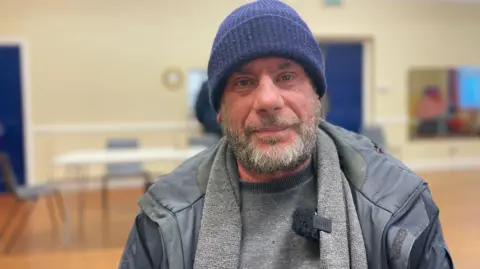 Mark NormanBBC Paul smiles while sitting in a rough sleepers winter shelter