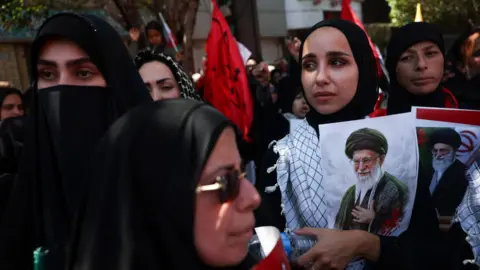 WANA via Reuters Mourners hold photos of Iran's late Supreme Leader Ayatollah Ali Khamenei ahead of his burial in Mashhad, north-eastern Iran (9 July 2026)