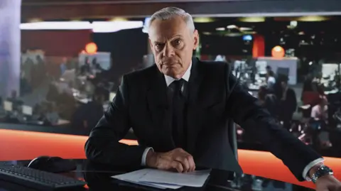 5 Broadcasting Limited / Paramount / Wonderhood Studios/ PA Actor Martin Clunes depicted as former BBC presenter Huw Edwards. Clunes is photographed in character wearing a black suit and silver watch. The actor is sat in a newsroom studio with pieces of paper in front of him and a newsroom with journalists working behind him.