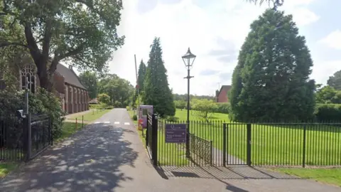 Google Part of the Queenswood grounds. There is a gated entrance, an ornate building, and a large tree on the lawn.