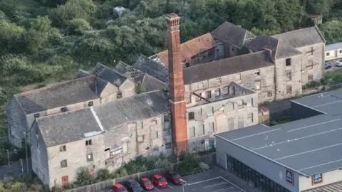 An aerial photo of the Baily's Buildings complex including multiple grey derelict buildings and a red tower, which are located next to an Aldi supermarket and car park
