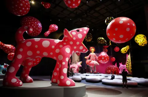 Reuters A series of large colourful polka dot sculptures in a dark gallery including a cat, a girl and balls