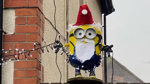 Mark Ryan The minion is on a fence dressed as Santa Claus with lights dangling off him. 