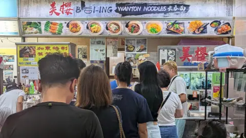 People stand in line in front of Bei-Ing Wanton Noodle stall in Singapore