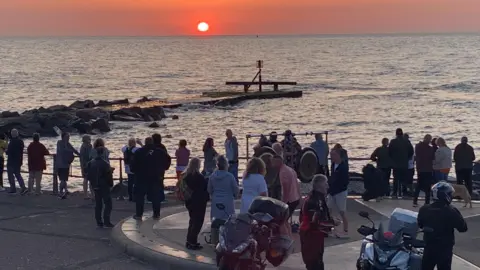 People stood looking out to sea from the UK's most easterly point in Lowestoft, with some motorcyclists in the foreground