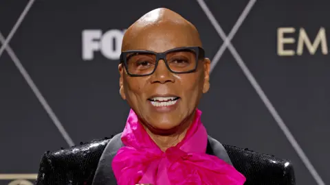 Getty Images A close up of RuPaul in a black suit with a pint neckerchief. 