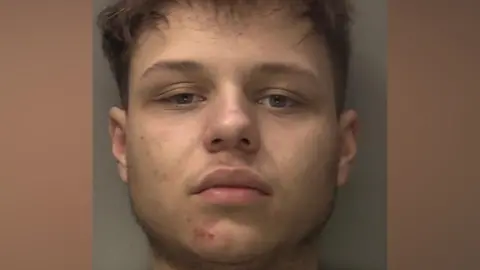 A police mug-shot of Corey Brown who has dark hair and is looking straight ahead. 