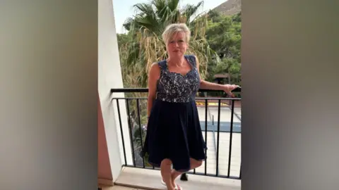 Family handout A blonde woman with a fringe wearing a dress smiles as she stands on a balcony. 