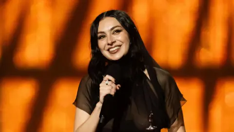 Charli XCX smiles holding microphone