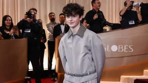 Owen Cooper, wearing a grey outfir, poses for photos at the Golden Globes award ceremony