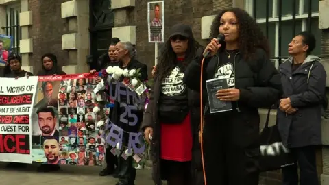 A woman holding a microphone with several other people standing behind her holding banners