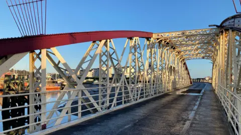 The road on the Swing Bridge, which has an arching red metal structure with white metal railings and a road.