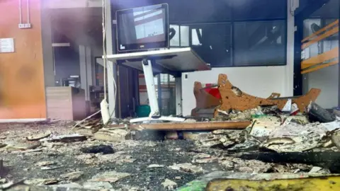 A photo of the library's interior, taken through the window, showing burnt debris on the ground