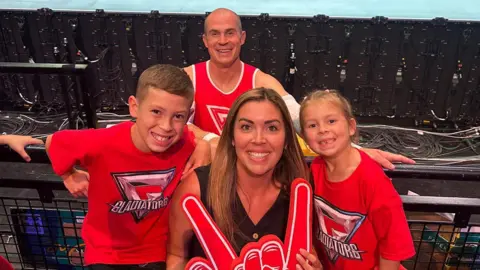 Supplied Two children and their mum with gladiator t-shirts and a foam hand, their dad is in the background behind the railing, dressed in the Gladiator vest