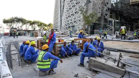 Getty Images Migrant Builders beristirahat saat bekerja di lokasi konstruksi oleh Corniche, di Doha, pada 24 November 2022, selama turnamen sepak bola Piala Dunia Qatar 2022. 