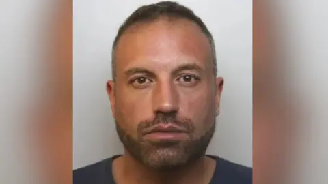 Avon and Somerset Police A police custody picture of Chalkley. He has short dark hair and a short beard, and wears a dark blue T-shirt.