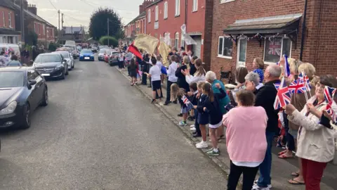 Several people standing on the pavement waiting for Maise to arrive 