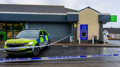 Pacemaker Police car in front of a shop with blue and white police cordons. An ATM is behind, which has been removed from the wall.